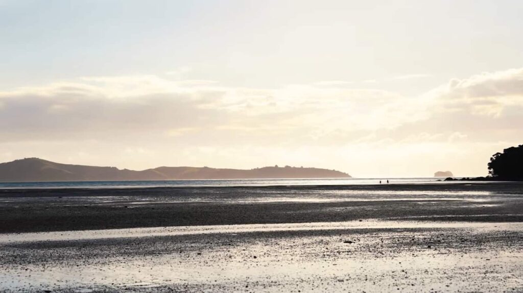 A vast beach at low tide under a soft sunset with distant figures