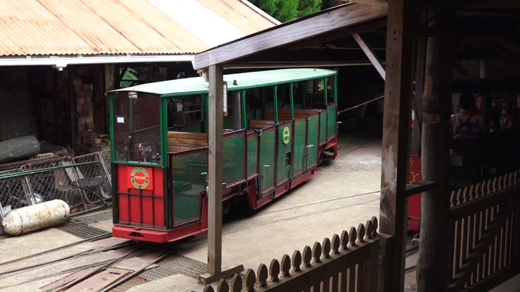 A green and red tram in a rustic station with passengers aboard